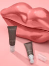 Två targeted lip filler står framför en rosa bakrund.