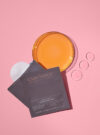 Exuviance produkten pure retinol correcting peel mot en rosa bakrund med ingredienser runt omkring.