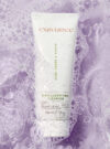 Exuviance produkten 3-in-1 clarifying cleanser ligger i ett skummat vatten med en lila bakrund.