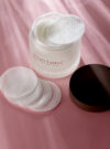 Exuviance produkten daily resurfig peel presenteras mot en rosa bakrund.