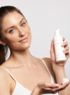 En Exuviance kvinna ler mot kameran och håller upp produkten bioactiv wash med en hand och har pumpat ut produkten i den andra handen.