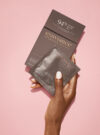 En hand håller upp exuviance produkten pure retinol correcting peel mot en rosa bakrund.