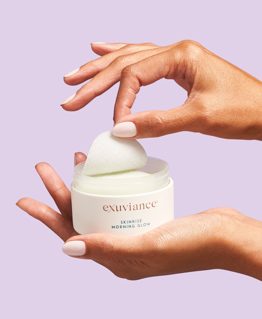 Foto av två händer som håller upp produkten SkinRise Morning Glow och tar upp en pad ur burken.