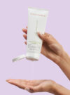 Två händer som trycker ut produkten 3-in-1 clarifying cleanser mot lila bakrund.