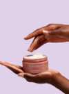 Två händer håller upp produkten advanced toning neck cream mot lila bakrund.