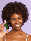 Exuviance kvinna ler stort mot kameran och håller upp produkten radiance serum.
