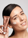 Exuviance kvinna ler mot kameran med produkten day repair SPF 30 intill ansiktet och har krämen på kinden.
