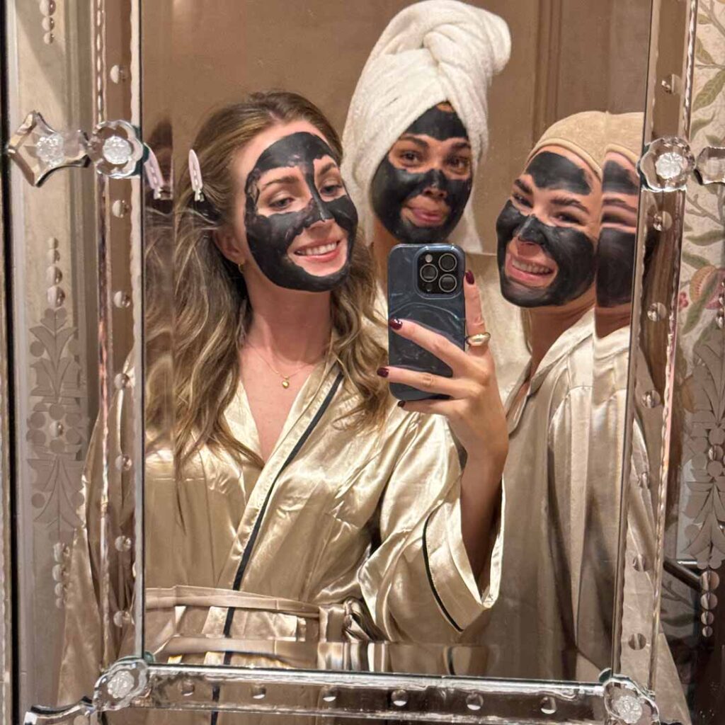Foto av tre unga kvinnor som har Exuviance ansiktsmask på sig och tar en selfie i en spegel.