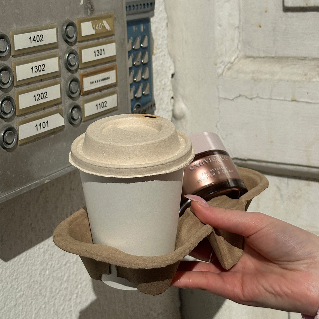 Foto av Exuviance Rebuild-5 Cream med en take away-kaffe framför en porttelefon.