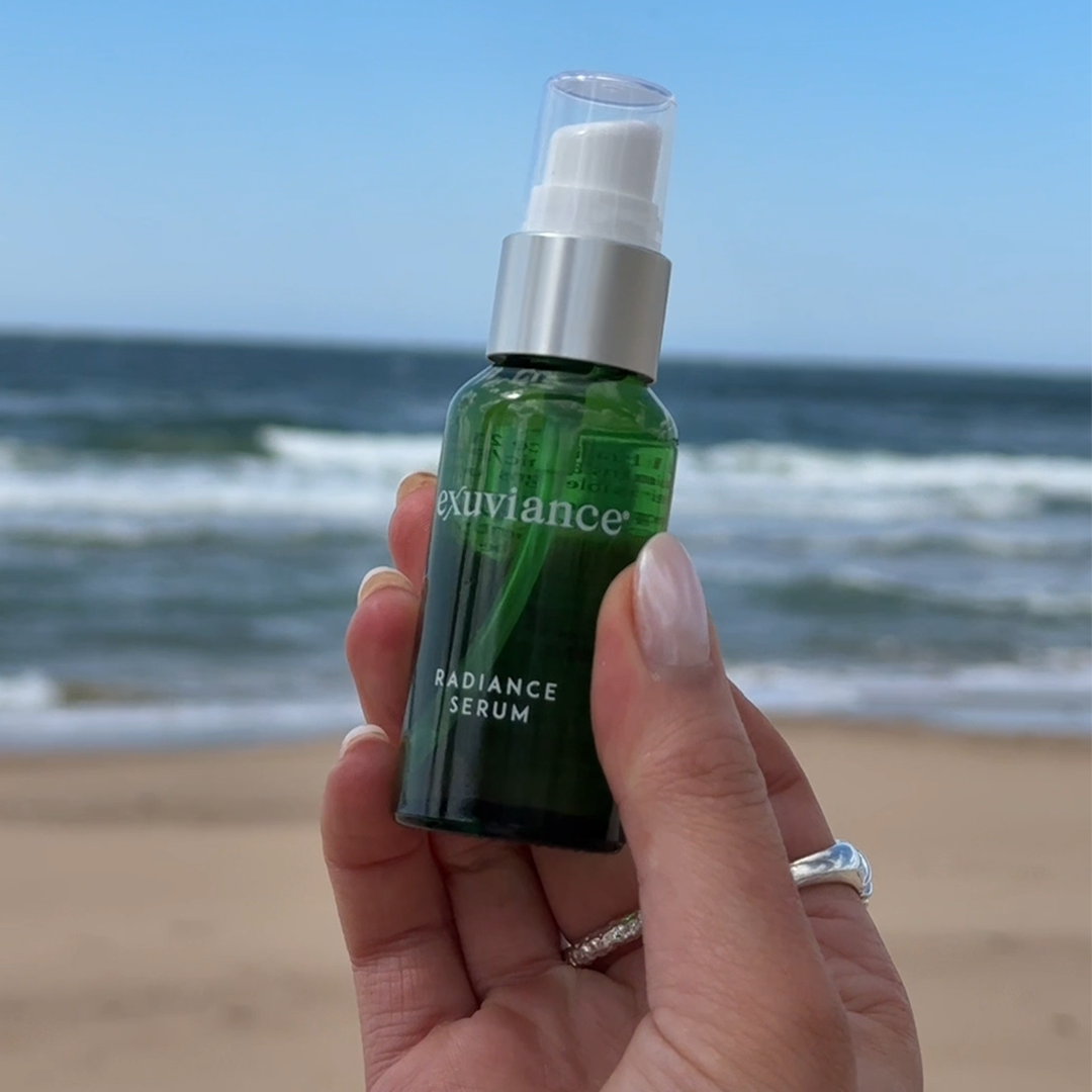 Hand som håller upp Radiance Serum framför havet.